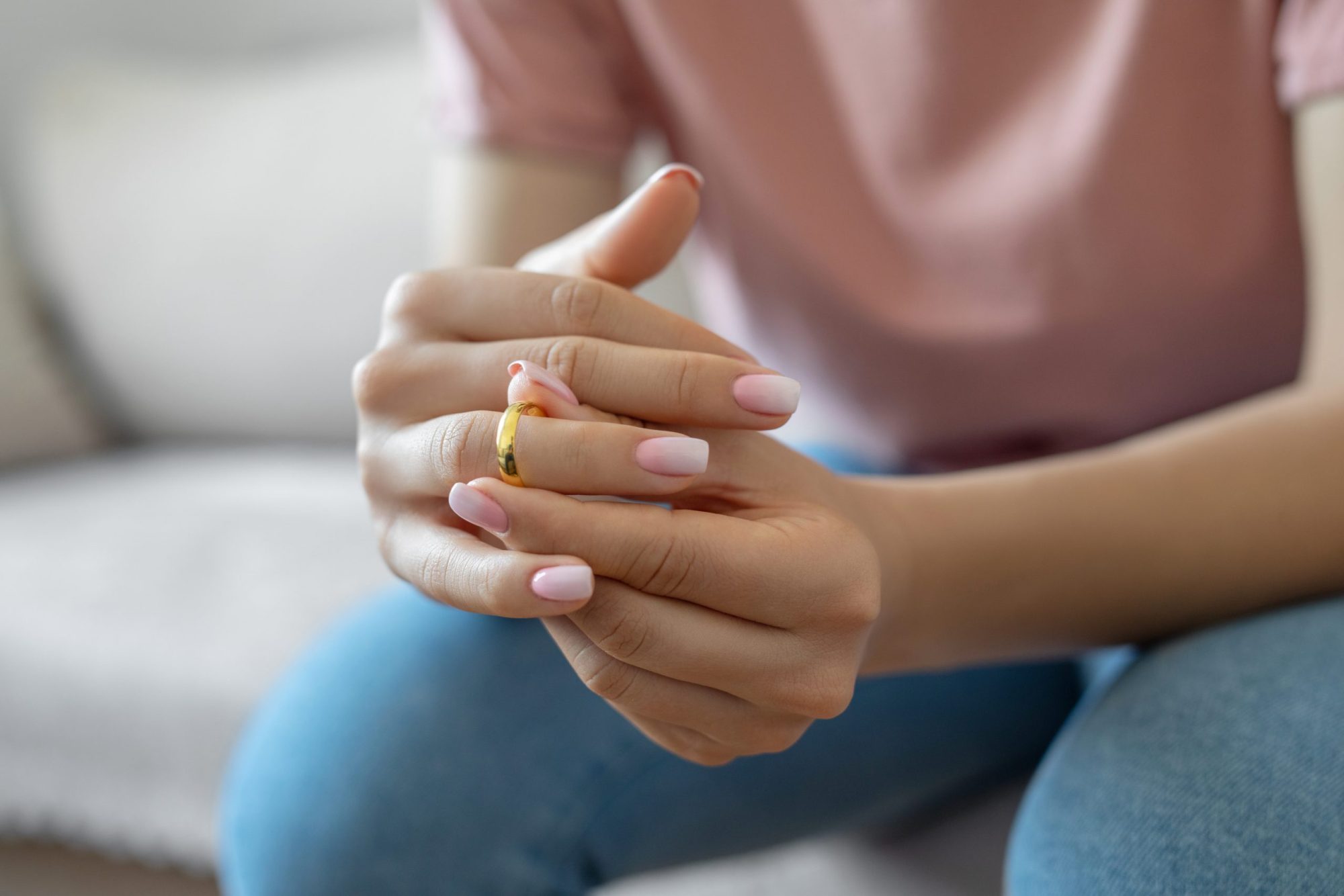 Close up on a woman, sitting, her hands clasped together as she nervously fidgets with her wedding ring.